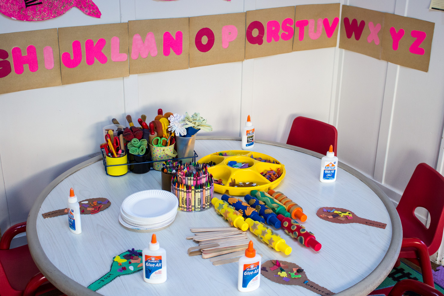 The craft table at Shining Stars, set with a crayon caddy, glue bottles, and a paper alphabet banner on kraft paper.
