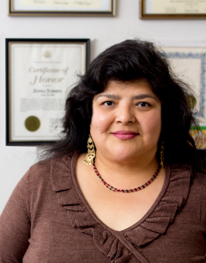 Zonia Torres, owner and lead provider of Shining Stars Family Child Care, standing in front of her wall of framed certificates and training credentials.